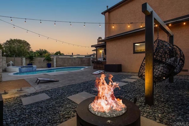 pool at dusk with an in ground hot tub, a patio, and a fire pit