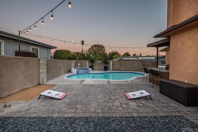 pool at dusk with an in ground hot tub, exterior bar, and a patio