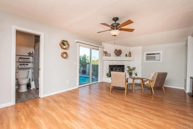 living room featuring ceiling fan, a stone fireplace, light hardwood / wood-style flooring, and an AC wall unit