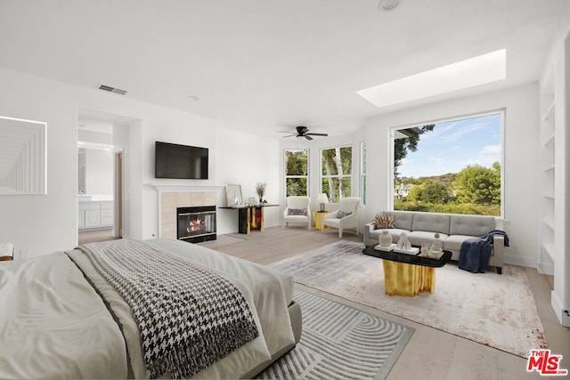 bedroom with multiple windows, ensuite bathroom, a tile fireplace, and light hardwood / wood-style flooring