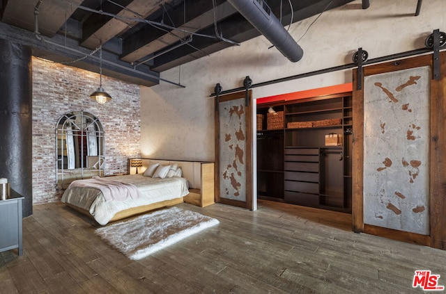 unfurnished bedroom featuring brick wall, a barn door, hardwood / wood-style floors, and a high ceiling