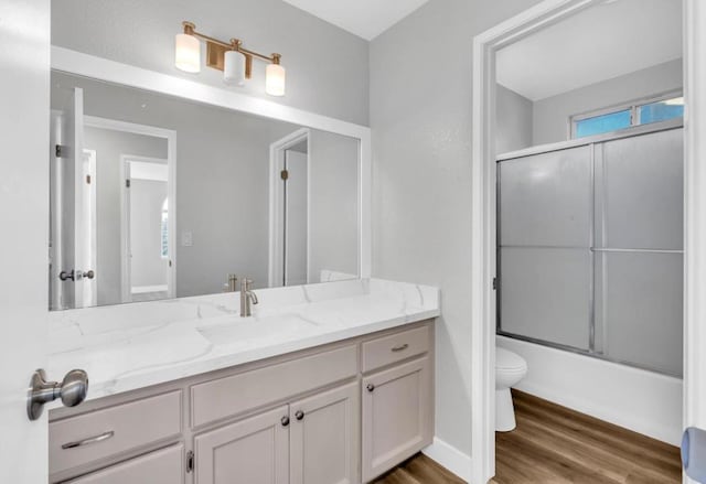 full bathroom with enclosed tub / shower combo, hardwood / wood-style floors, vanity, and toilet