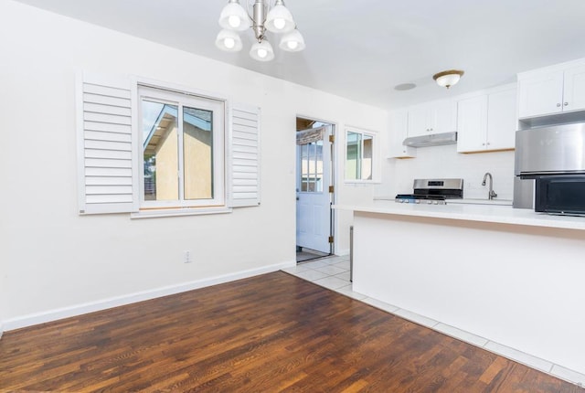 kitchen featuring stainless steel stove, refrigerator, white cabinetry, hanging light fixtures, and light hardwood / wood-style floors