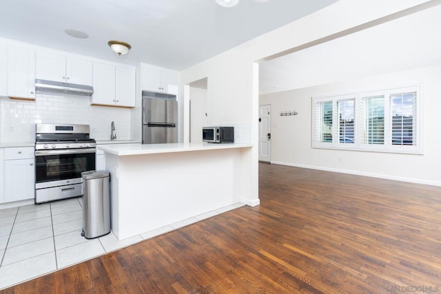 kitchen featuring appliances with stainless steel finishes, light wood-type flooring, decorative backsplash, and white cabinets