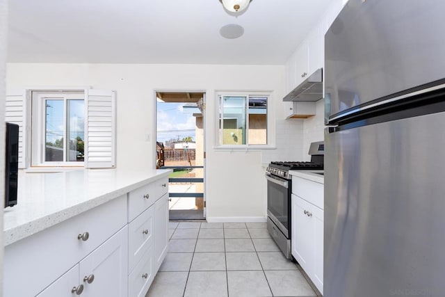 kitchen with backsplash, stainless steel appliances, light stone countertops, white cabinets, and light tile patterned flooring