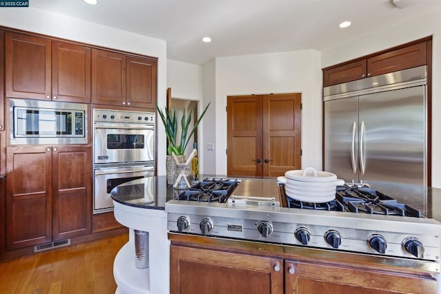 kitchen featuring dark hardwood / wood-style floors, dark stone counters, and built in appliances