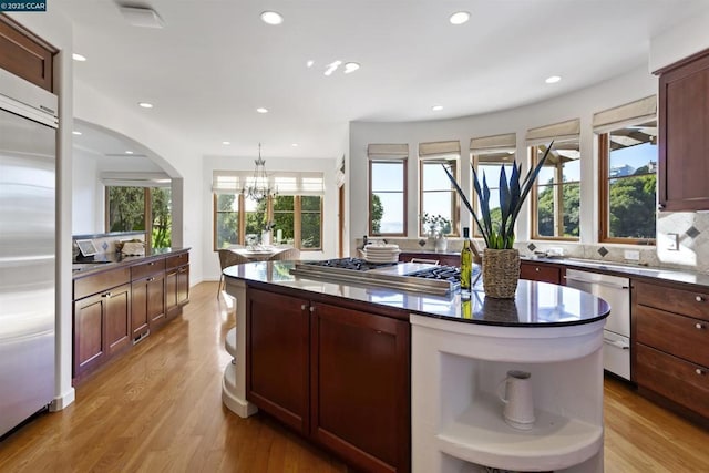 kitchen featuring decorative light fixtures, decorative backsplash, a center island, stainless steel appliances, and light wood-type flooring