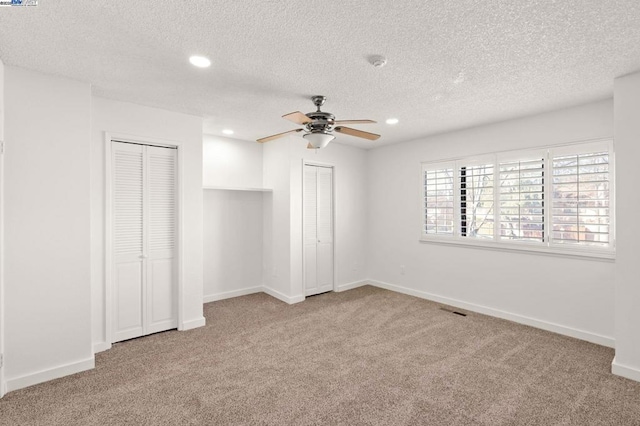 unfurnished bedroom with a textured ceiling, two closets, light colored carpet, and ceiling fan