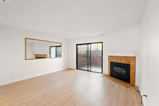 unfurnished living room featuring a tiled fireplace, light hardwood / wood-style flooring, and a textured ceiling