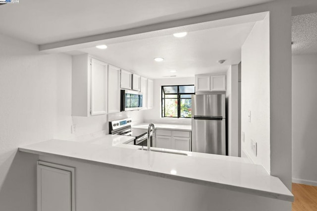 kitchen with sink, appliances with stainless steel finishes, white cabinets, kitchen peninsula, and light wood-type flooring