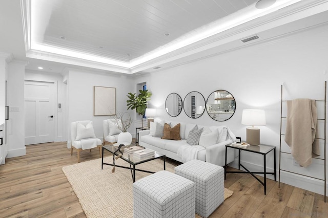 living room featuring crown molding, a raised ceiling, and light wood-type flooring