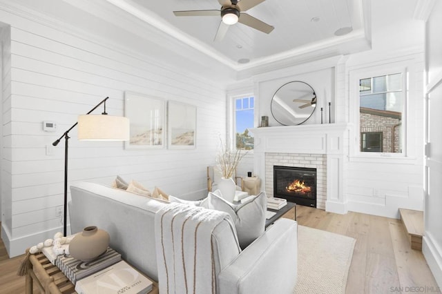 living room with a fireplace, ceiling fan, a raised ceiling, crown molding, and light hardwood / wood-style flooring