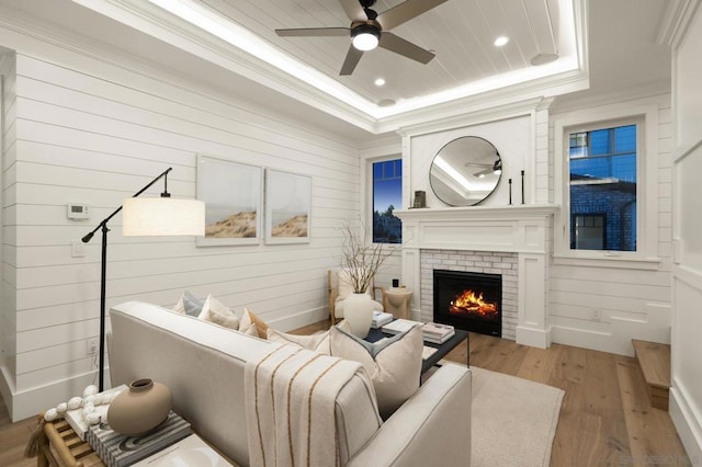 living room with a fireplace, ornamental molding, ceiling fan, light hardwood / wood-style floors, and a raised ceiling