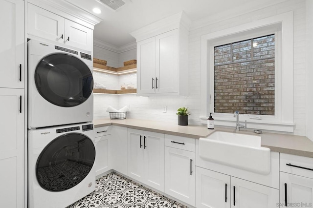 laundry room featuring stacked washing maching and dryer, sink, cabinets, ornamental molding, and light tile patterned floors