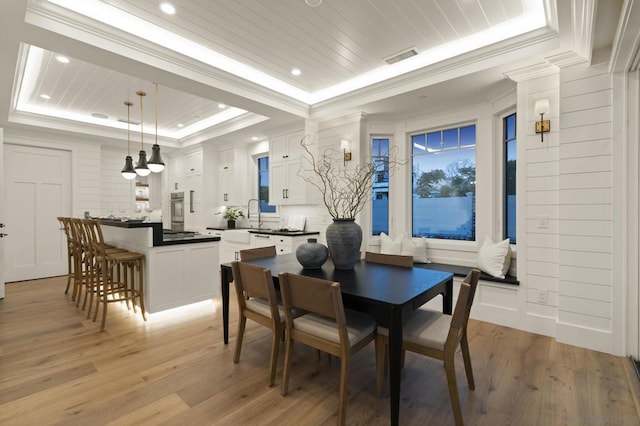 dining area with sink, ornamental molding, wooden ceiling, a raised ceiling, and light wood-type flooring