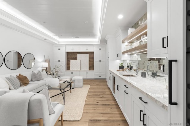 living room with ornamental molding, sink, a raised ceiling, and light hardwood / wood-style floors