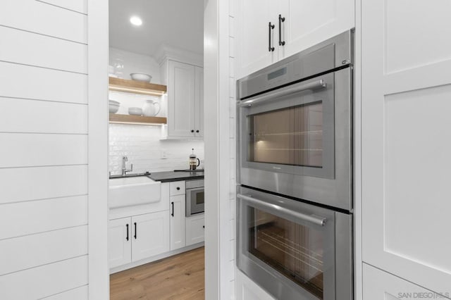 kitchen featuring sink, light wood-type flooring, double oven, white cabinets, and backsplash