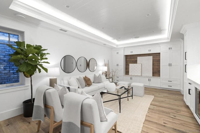 living room with ornamental molding, a raised ceiling, and light wood-type flooring