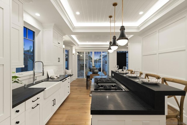 kitchen with decorative light fixtures, sink, white cabinets, ornamental molding, and a raised ceiling