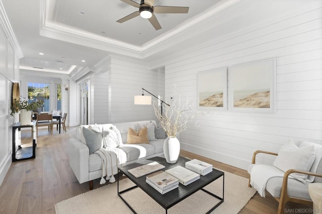 living room with a raised ceiling, crown molding, hardwood / wood-style flooring, and ceiling fan