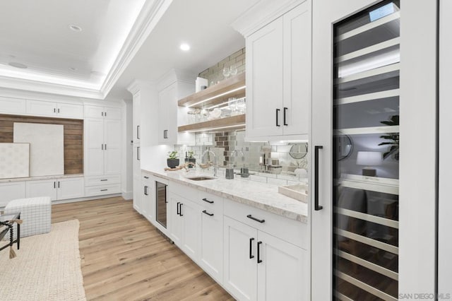 bar featuring sink, white cabinetry, a tray ceiling, light stone countertops, and beverage cooler