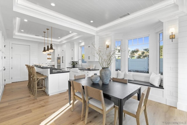 dining area with crown molding, a tray ceiling, and light hardwood / wood-style flooring