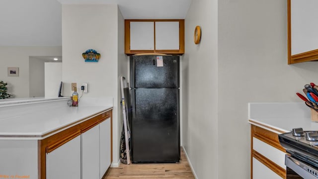 kitchen featuring black fridge, white cabinetry, and light wood-type flooring