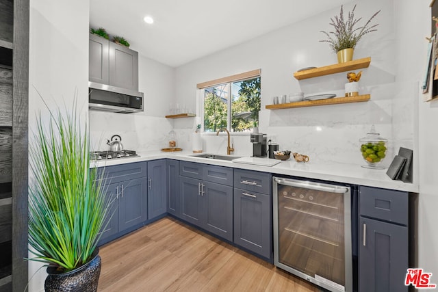 kitchen featuring wine cooler, sink, tasteful backsplash, light wood-type flooring, and stainless steel appliances