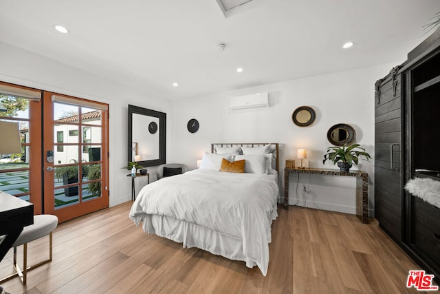 bedroom featuring a barn door, a wall mounted AC, access to exterior, and light hardwood / wood-style flooring