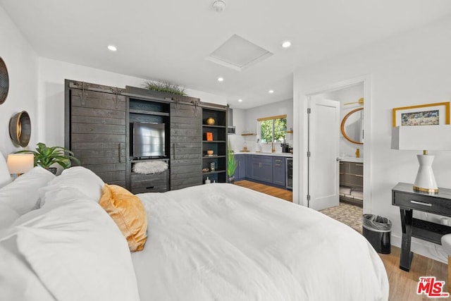 bedroom with beverage cooler, ensuite bath, and light hardwood / wood-style flooring