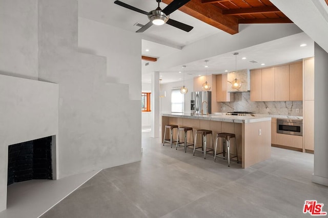 kitchen featuring appliances with stainless steel finishes, light brown cabinetry, decorative light fixtures, backsplash, and a center island