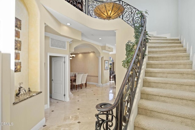 staircase with crown molding, decorative columns, and a high ceiling