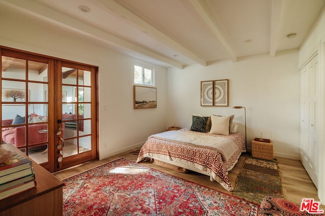 bedroom with beamed ceiling, light hardwood / wood-style flooring, and french doors