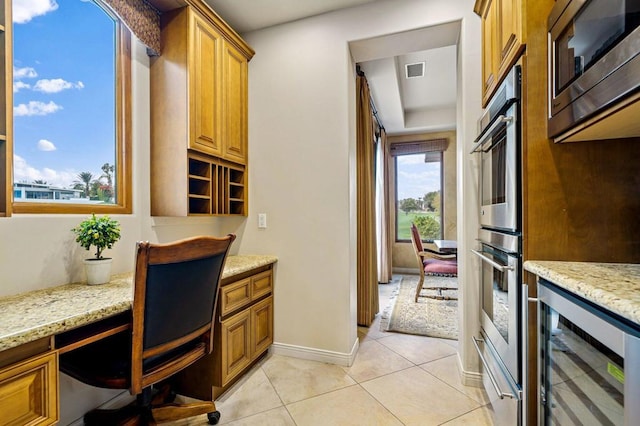 kitchen featuring built in desk, light tile patterned floors, stainless steel appliances, beverage cooler, and light stone countertops