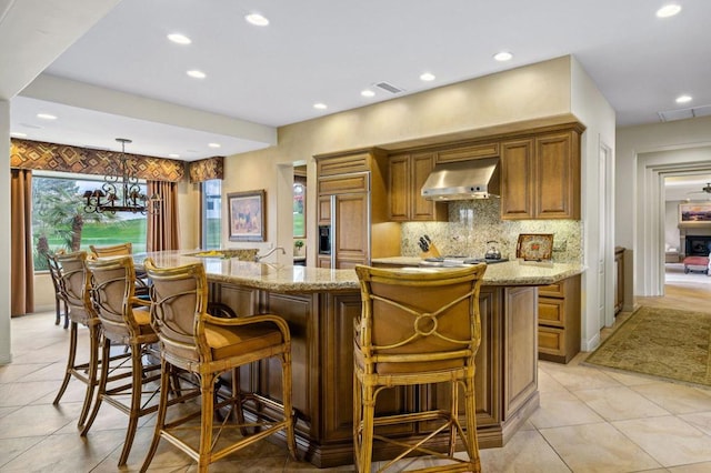 kitchen with hanging light fixtures, extractor fan, a large island, and paneled built in refrigerator