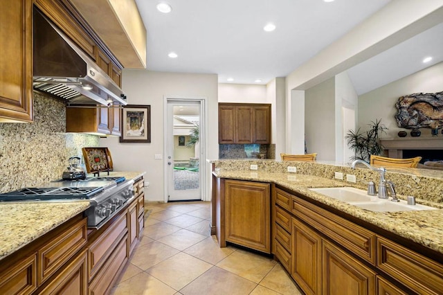 kitchen with stainless steel gas cooktop, sink, light stone countertops, and extractor fan