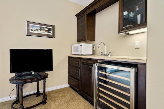 bar with wine cooler, dark brown cabinets, sink, and light carpet