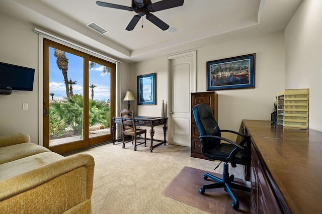 home office with ceiling fan, carpet flooring, and a tray ceiling