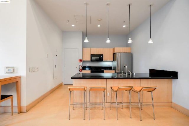 kitchen with a breakfast bar, a towering ceiling, stainless steel refrigerator, sink, and light brown cabinets