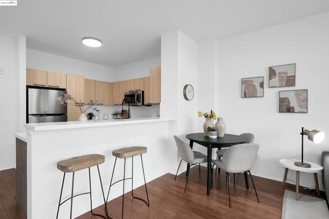 kitchen with dark wood-type flooring, stainless steel appliances, kitchen peninsula, and light brown cabinets