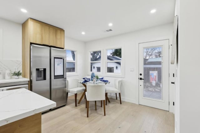 kitchen featuring light stone counters, light wood-type flooring, and stainless steel refrigerator with ice dispenser