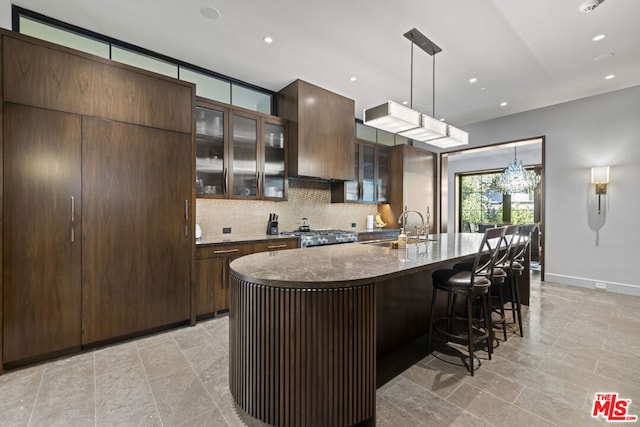 kitchen with sink, stove, hanging light fixtures, backsplash, and an island with sink