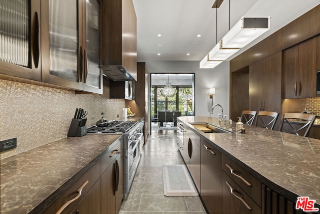 kitchen featuring sink, hanging light fixtures, dark brown cabinets, tasteful backsplash, and high end stove