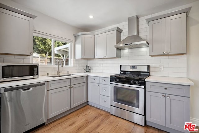 kitchen with sink, appliances with stainless steel finishes, gray cabinetry, wall chimney exhaust hood, and light wood-type flooring