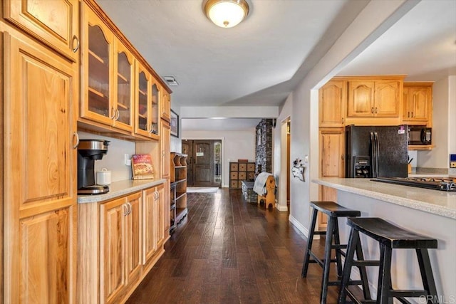 kitchen featuring light stone counters, dark wood-type flooring, a breakfast bar area, and black appliances