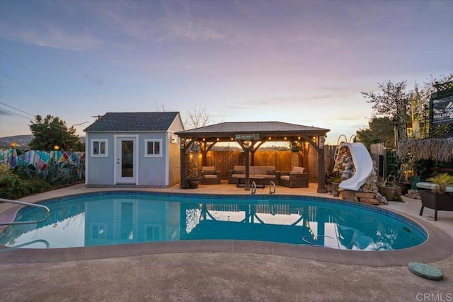 pool at dusk with a gazebo, a water slide, an outbuilding, an outdoor hangout area, and a patio