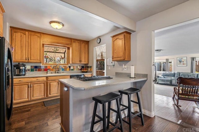 kitchen featuring black fridge, dark hardwood / wood-style floors, sink, and a breakfast bar area