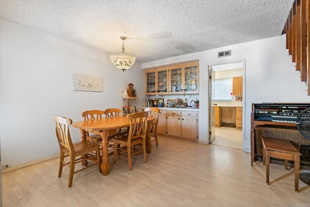 dining area featuring an inviting chandelier, a textured ceiling, and light wood-type flooring