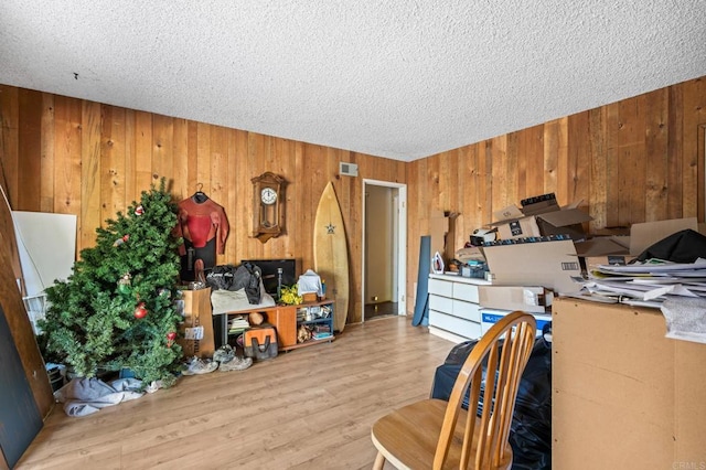 misc room with wood walls, a textured ceiling, and light wood-type flooring