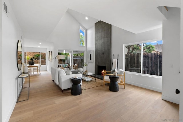 living room featuring a fireplace, high vaulted ceiling, and light wood-type flooring